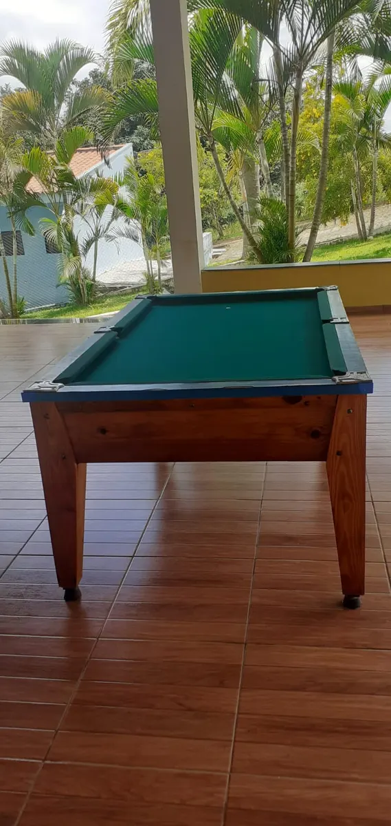 Mesa de bilhar em área coberta com vista para o jardim e palmeiras